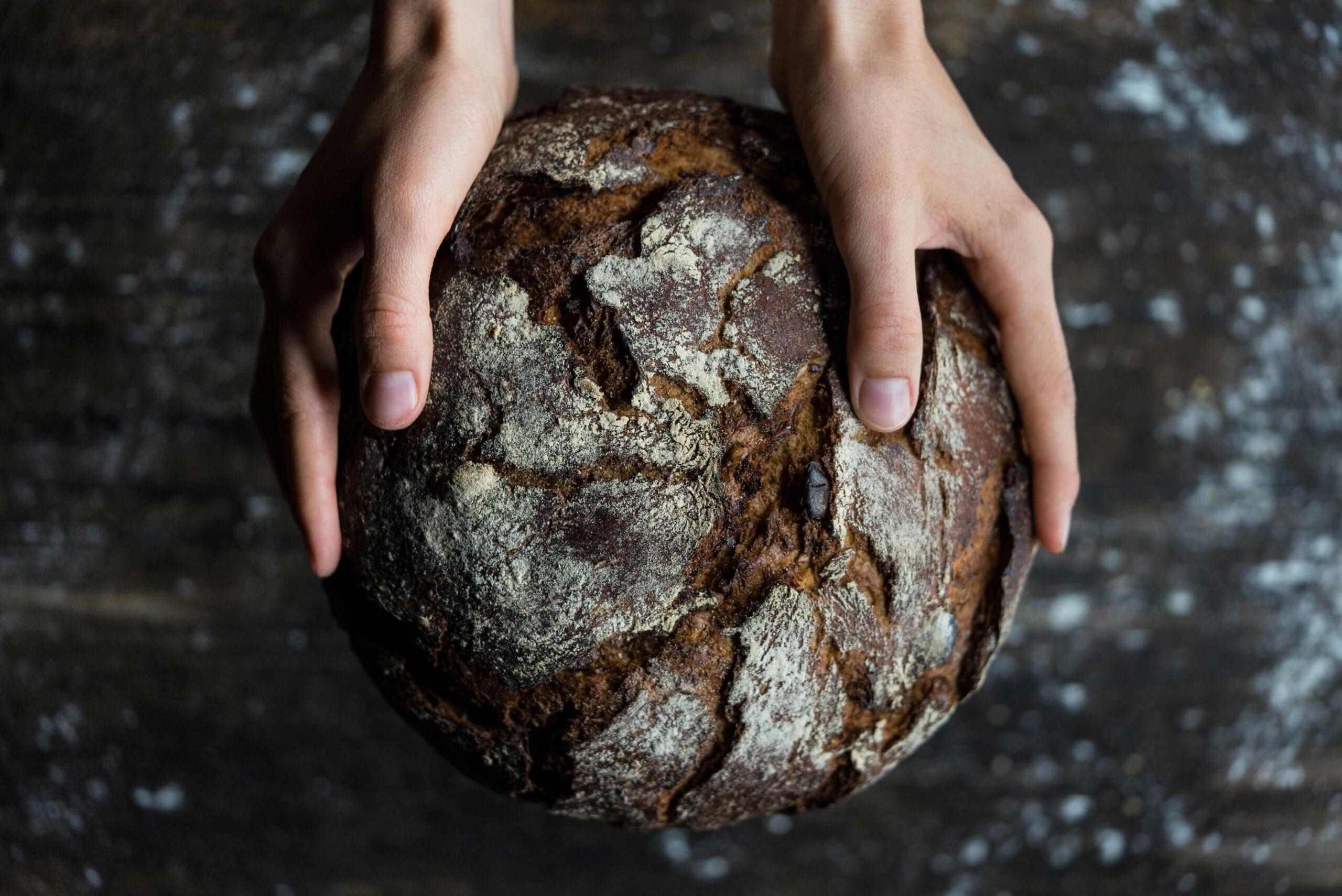 Baker's Percentage: Bake with Precision 1 Close-up of hands holding a rustic loaf of whole wheat bread with a dark, textured crust.